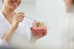 Female dentist pointing to model of dental implant